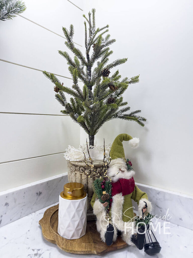 In the bathroom a wooden charger holds a small pine tree in a thrifted pot, embellised with vintage doilies, and a vintage santa in a green suit.