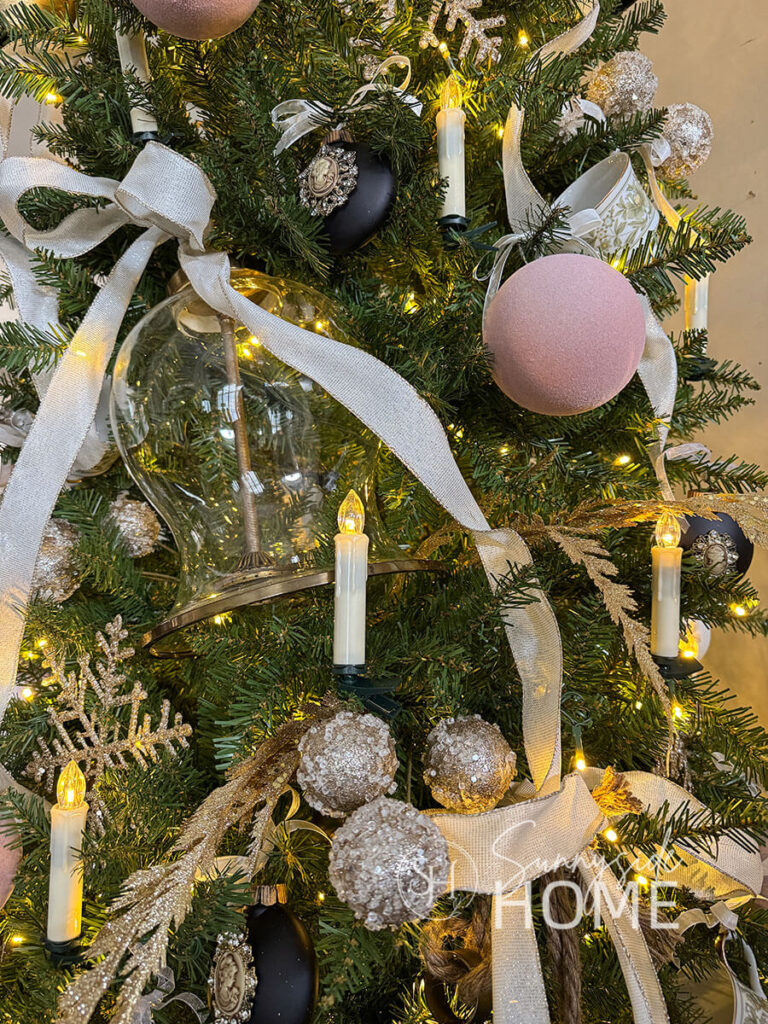 Close up view of the Christmas tree ornaments, dusty pink velvet balls, cameo ornaments, candles, glitter snowflakes, large bell, and teacups all tied to the Christmas tree with pretty ribbon.