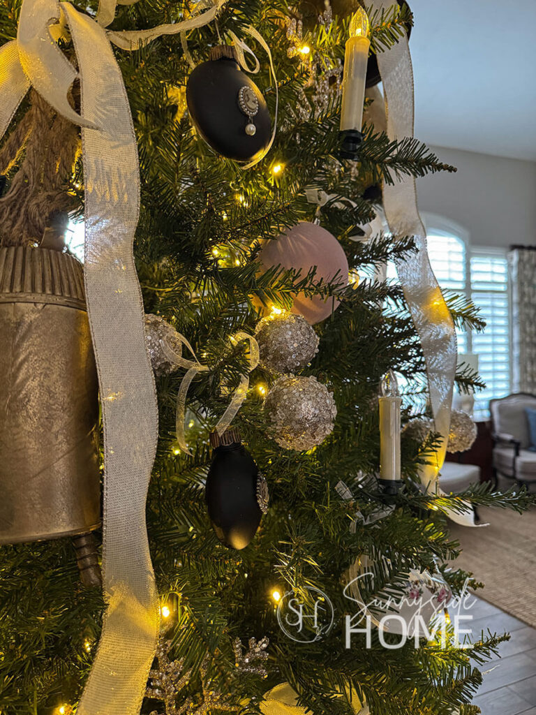 Close up view of the Christmas tree ornaments, dusty pink velvet balls, cameo ornaments, candles, glitter snowflakes, large brass bells, and teacups all tied to the Christmas tree with pretty ribbon.