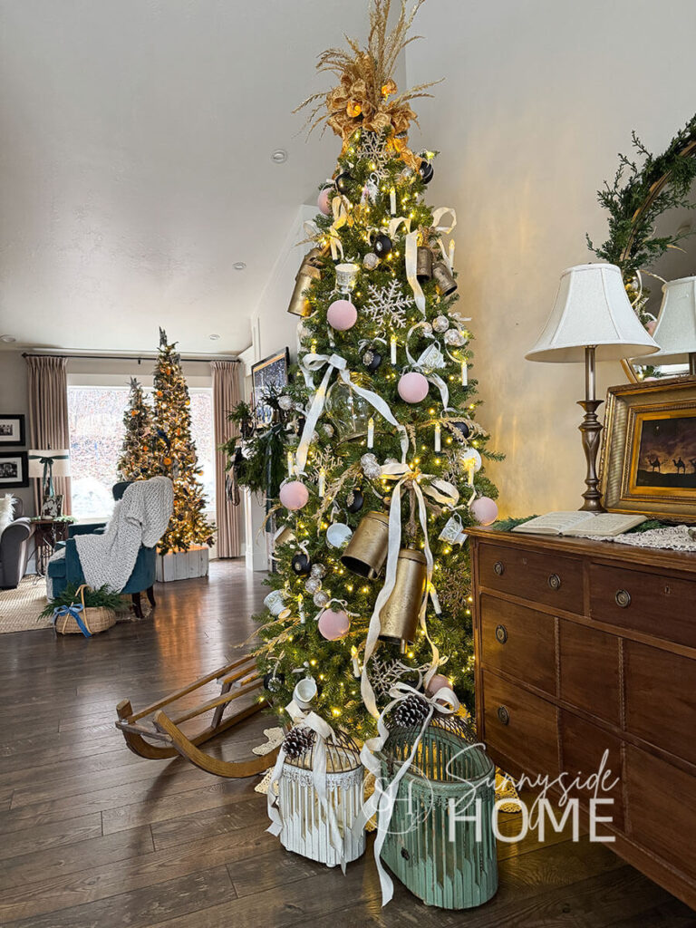 Entryway with a 9' Yorkshire pine tree decorated with pink velvet balls, large glitter snowflakes, large DIY faux brass bells, cameo ornaments all tied to the tree with pretty ivory and gold ribbon. An antique sled and birdcages are placed around the base of the Christmas tree.