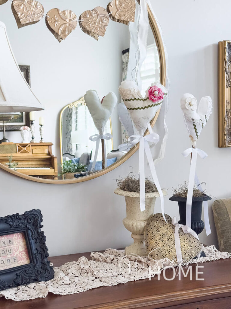 DIY Valentine heart decor styled on an entry table with faux vintage tile heart garland, brassed heart and vintage crochet table runner.