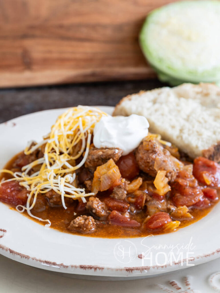 Easy beef and cabbage soup garnished with shredded cheese and sour cream, served with a slice of sour dough bread
