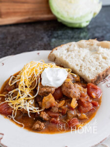 Feature image easy beef and cabbage soup garnished with shredded cheese and sour cream, served with a slice of sour dough bread