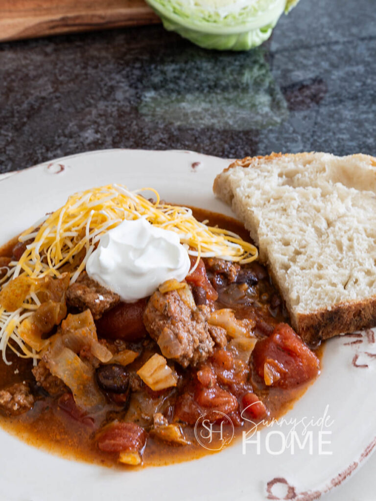 Easy beef and cabbage soup garnished with shredded cheese and sour cream, served with a slice of sour dough bread