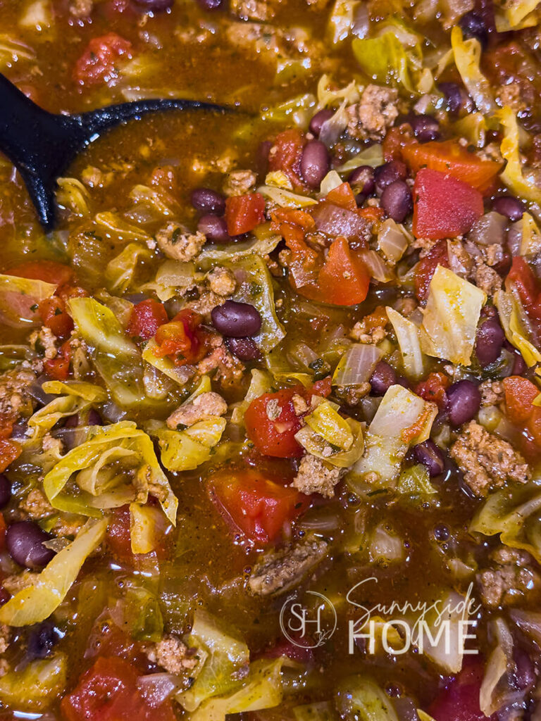 Cooked beef and cabbage soup with a serving spoon in a pot. The soup features savory ground beef seasoned with chili powder, diced tomatoes with chipotle peppers, black beans.