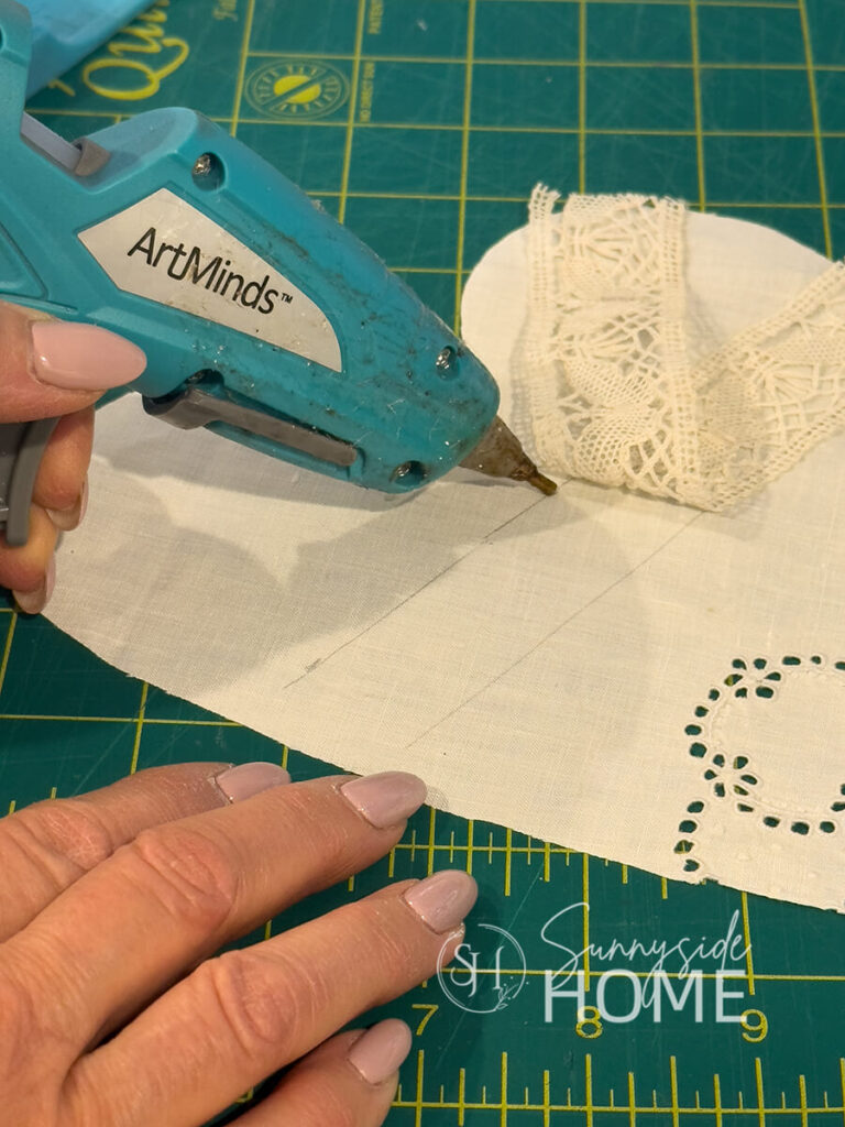 Woman applies a narrow bead of hot glue to vintage linen to adhere a piece of vintage lace.