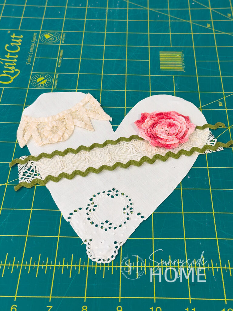 Vintage linens, trims and lace are placed on a heart shape cut from a vintage napkin to decide of placement of design.