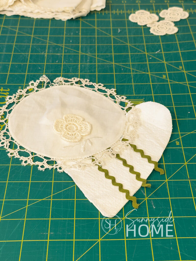 Vintage linens, trims and lace are placed on a heart shape cut from a vintage napkin to decide of placement of design.