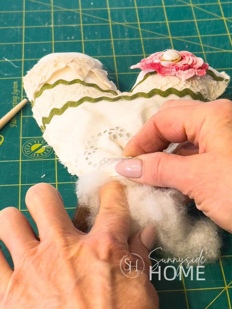 Woman stuffs a Valentine heart embellished with vintage lace and trim with polyfill.