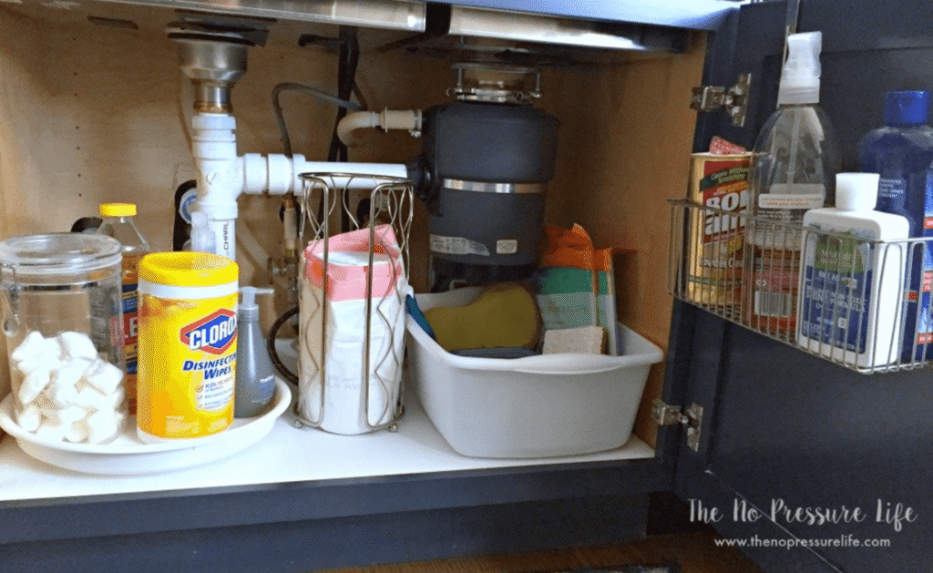 A toilet paper holder is used to store and organize a roll of trash bags. Other clever organizing under kitchen sink ideas include: a Lazy Susan to hold cleaning supplies, an over the cabinet door organizer and a plastic tub fits under the garbage disposal.