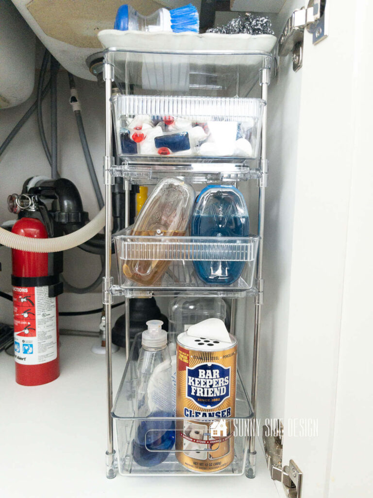 A narrow tiered organizer fits between the pipes under the sink.