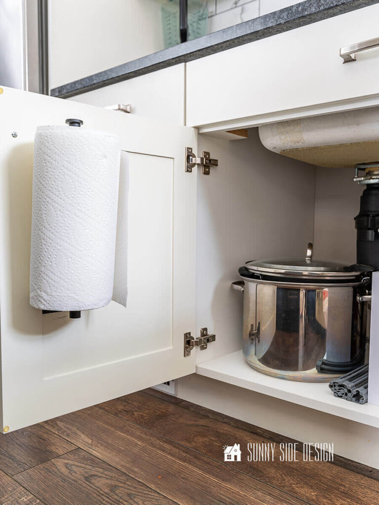 A paper towel holder is mounted to the inside of the cabinet door under the kitchen sink.