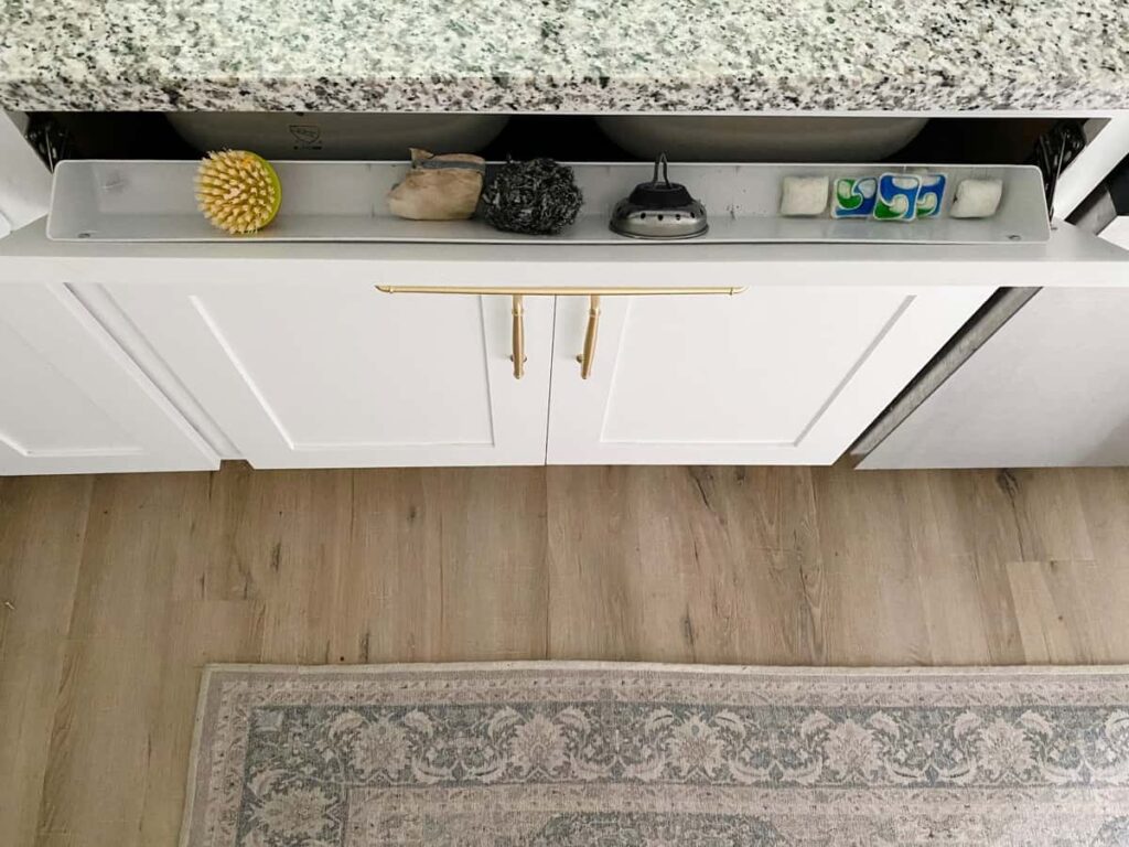 DIY Tilt out organizer with a cleaning brush, dishwasher tabs, strainer and scrubber.