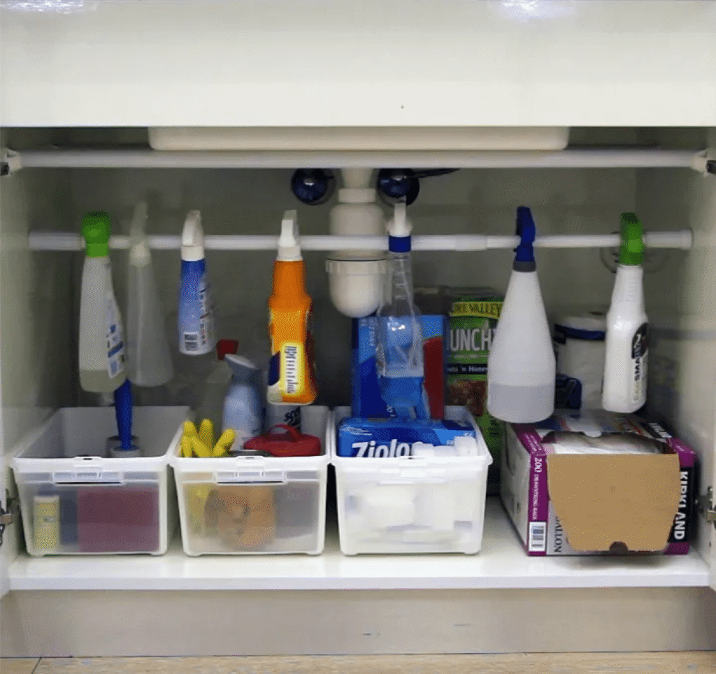 A tension rod us used under the kitchen sink to organize spray bottles of cleaning supplies.