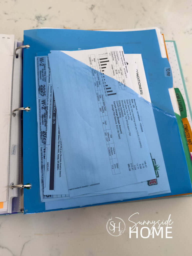 A binder is used to organize bills and documents that need attention with labeled pocket folders.