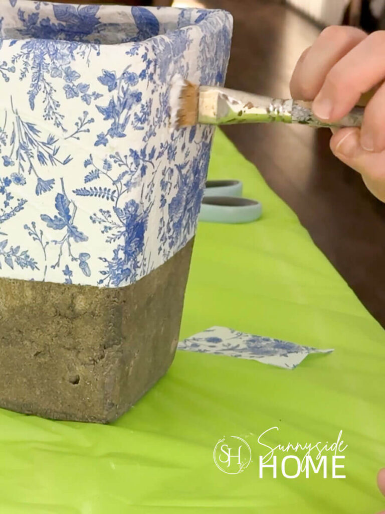 Mod Podge is applied over the blue and white napkins on a vase.