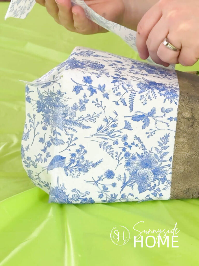 Woman demonstrates how to decoupage a vase with blue and white napkins.