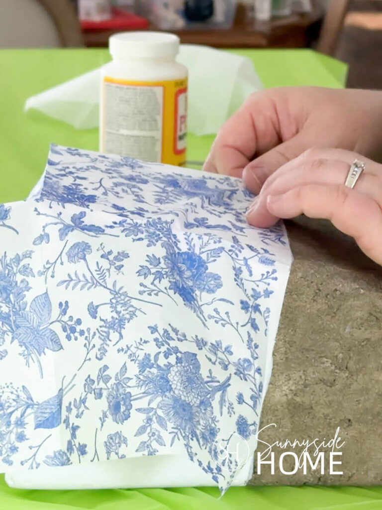 Woman demonstrates how to decoupage a vase with blue and white napkins.