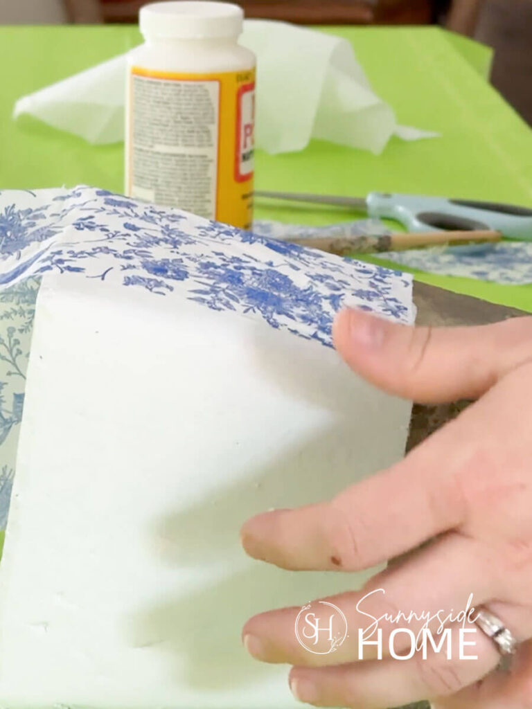 Woman demonstrates how to decoupage a vase with blue and white napkins.