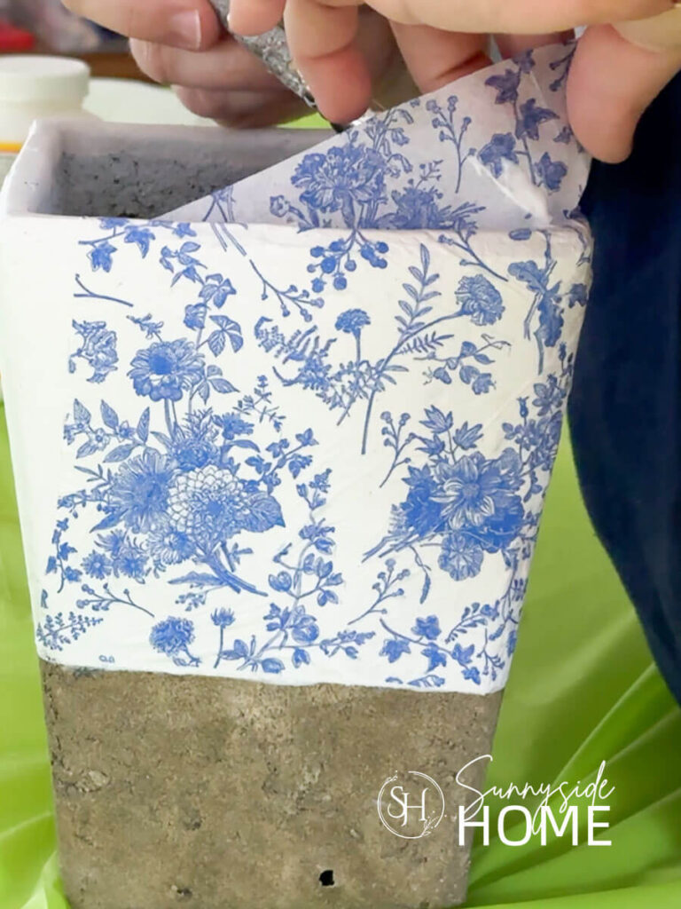 Decoupage medium is applied to the inside rim of a vase to adhere the napkin.
