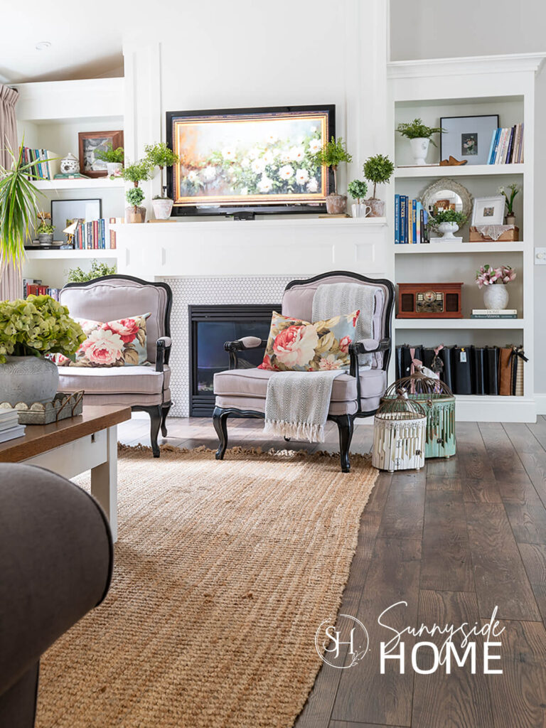 Floral pillow and throw blanket neatly placed in a light grey bergeré chair in a living room by the fireplace.