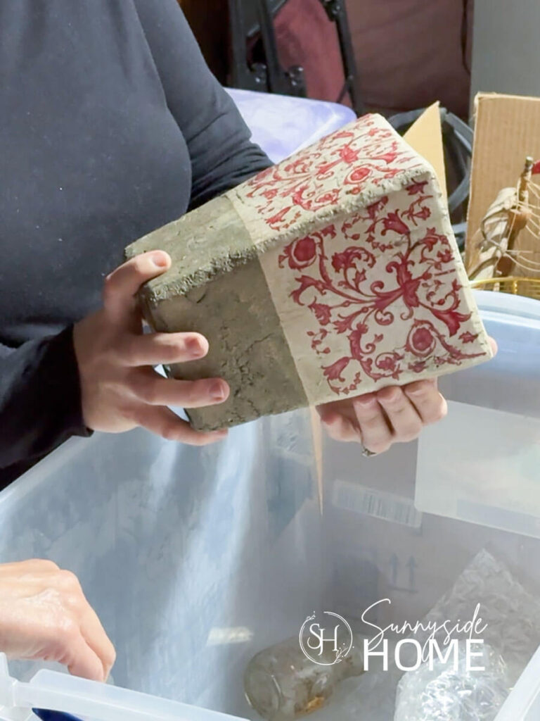 Woman pulls an old red and white patterned vase from a bin of old Home decor.