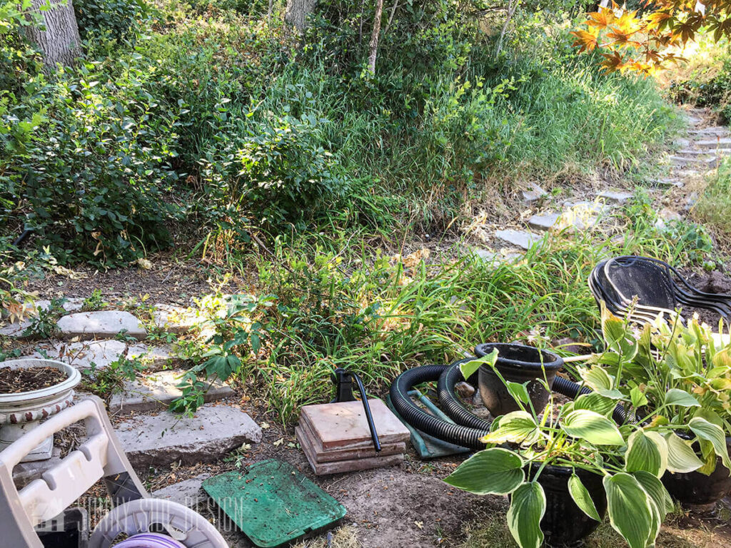 Backyard before makeover with a rustic path leading up the hill and weeds.
