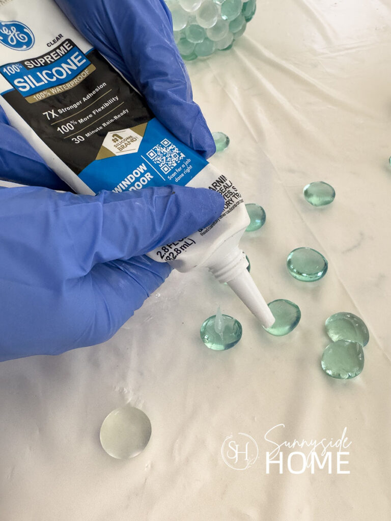 Woman applied clear silicone to the back of Dollar store glass gems.