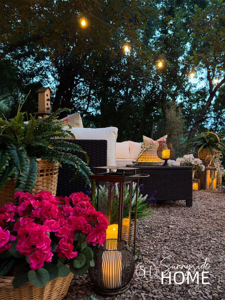 Beautiful outdoor living living room at dusk with lanterns and with glowing candles, overhead string lights, outdoor sectional, and planters.