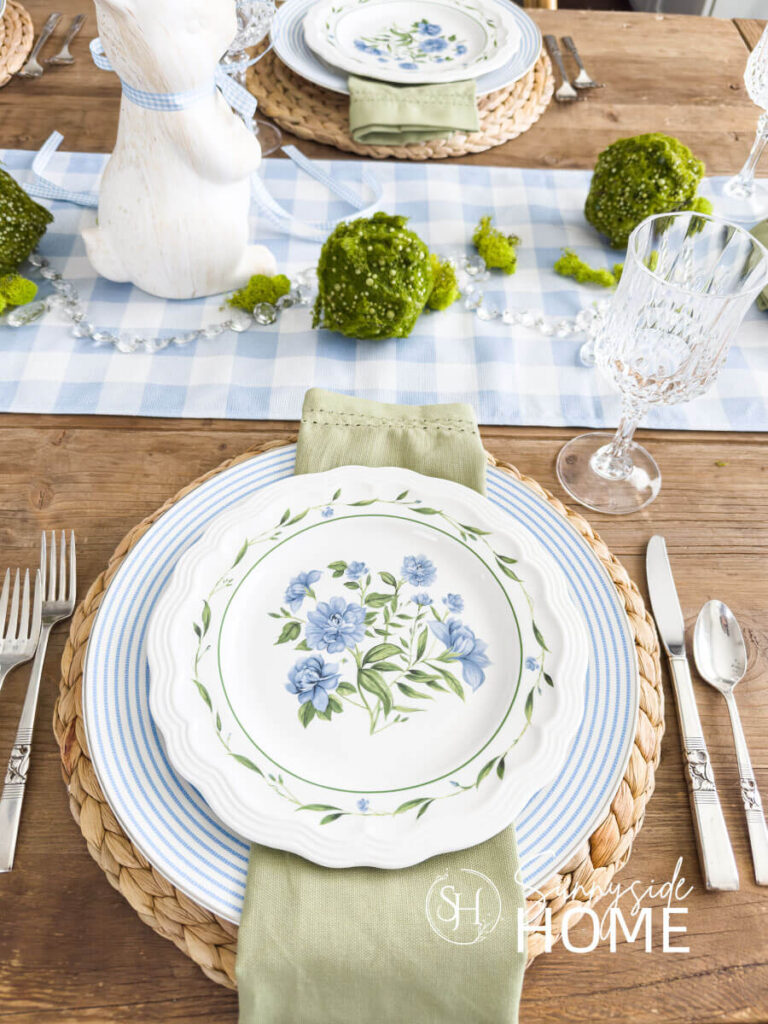 Blue and white Easter table settings water hyacinth placemats, blue and white striped plate, sage green napkin and a floral plate.