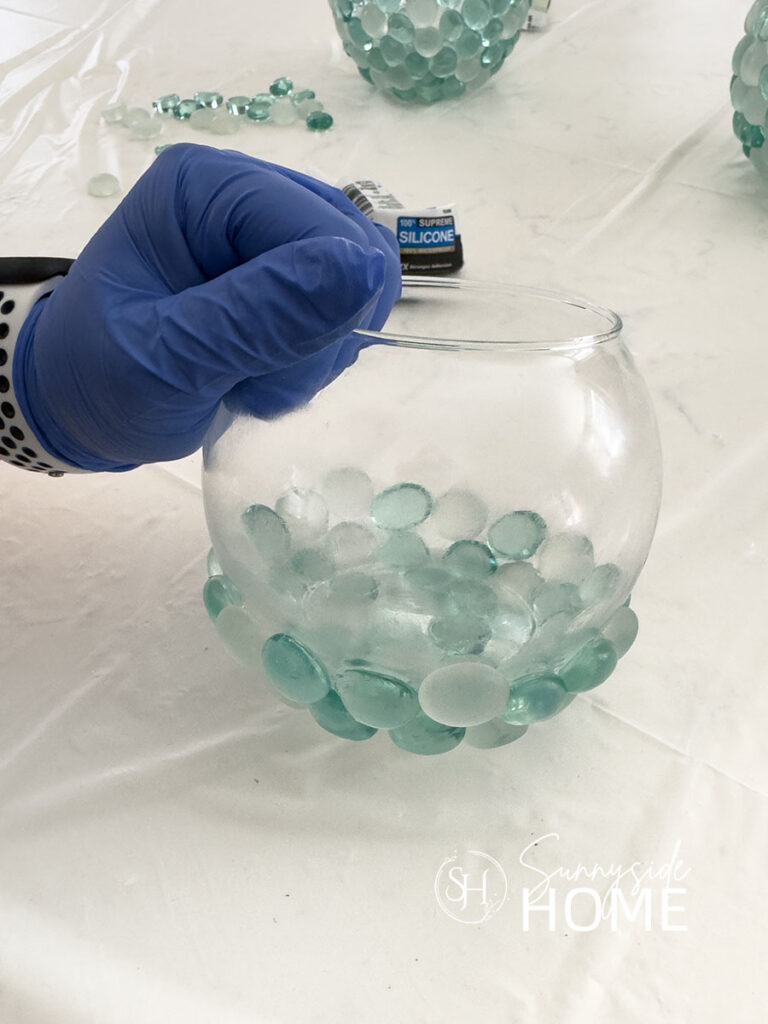 Woman holds a round dollar store glass vase that she had applied glass gems to with silicone.