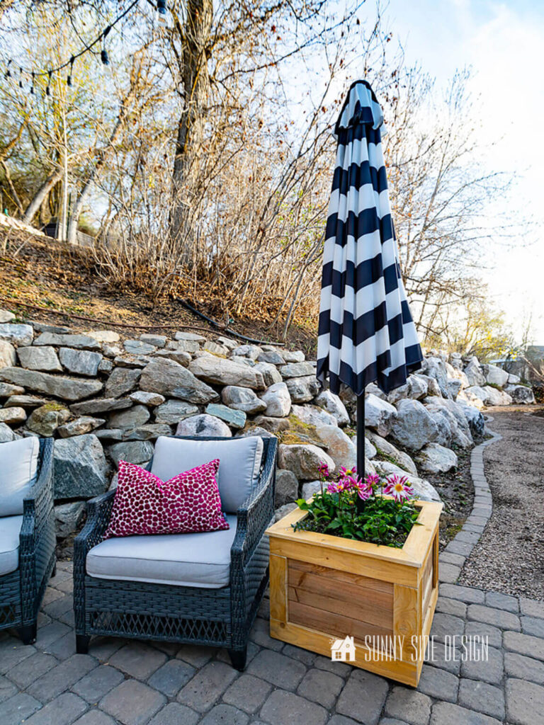 Mobile planter box with an umbrella provides adjustable shade in the patio, styled with wicker chairs.