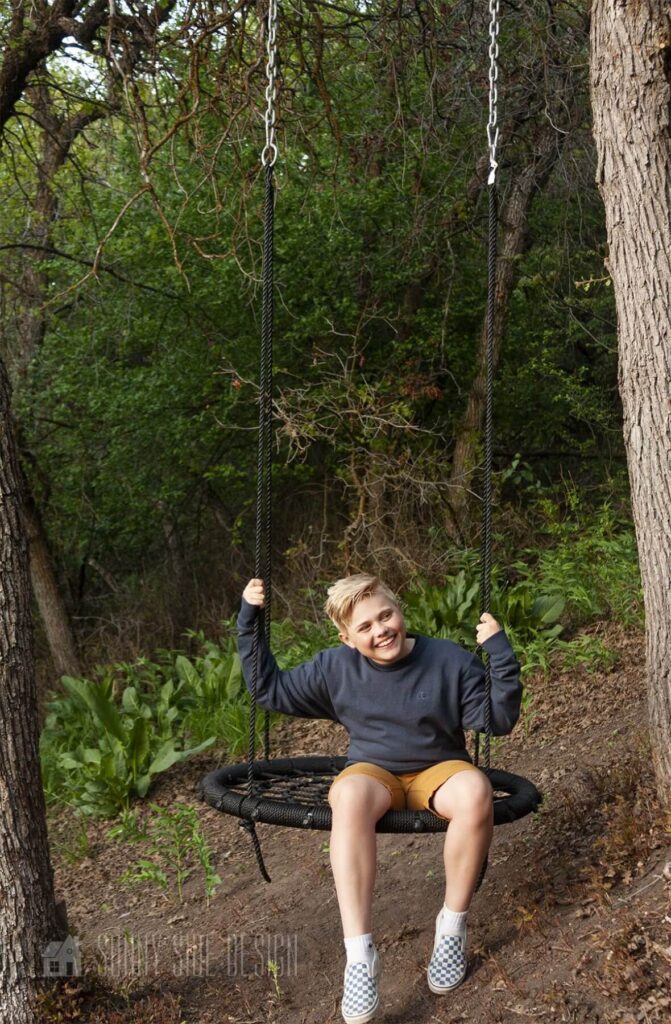 Boy sitting on a tree swing in the backyard.