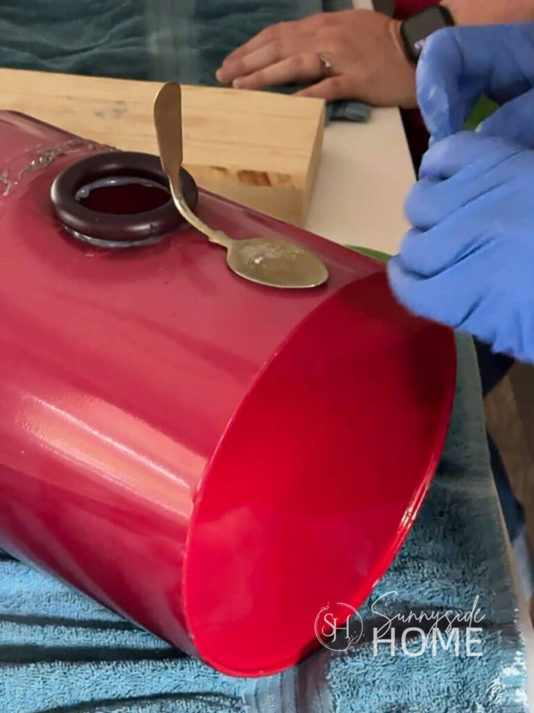 Woman attached a flattened and bent spoon to the red metal canister birdhouse with outdoor silicone for the perch.
