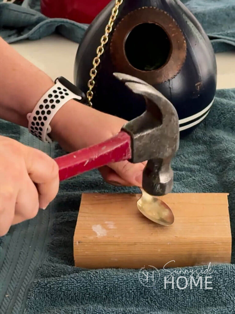 Woman hammers an old metal spoon to flatten it for the birdhouse perch.