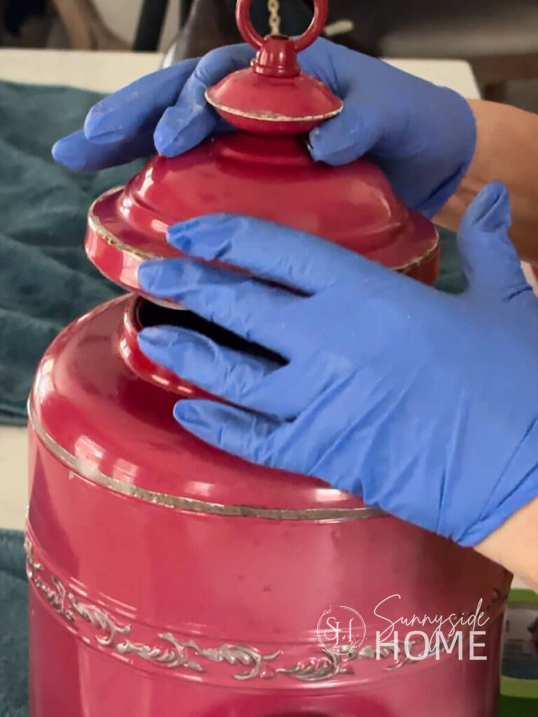 Woman attaches the metal lid to the red canister birdhouse with outdoor silicone.