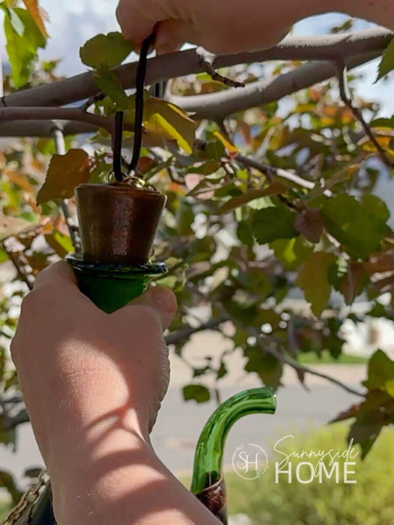 Woman hands whimsical birdhouse on a tree branch with a "S" hook.