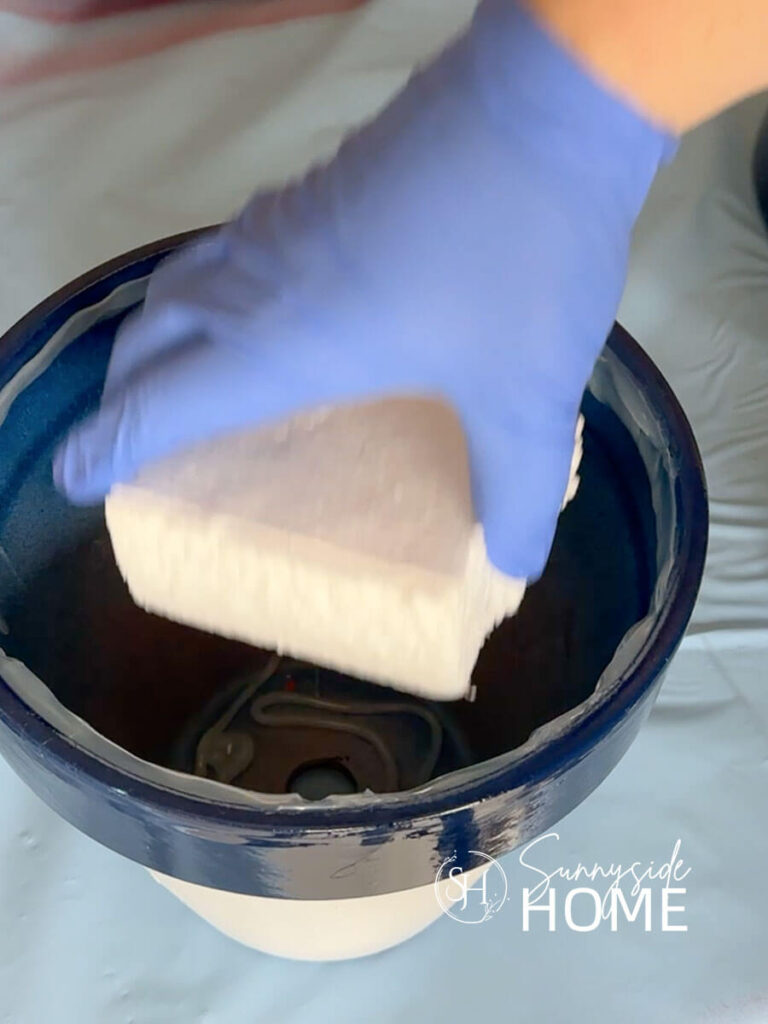 Woman placed a piece of styrofoam filler inside the painted clay pot.