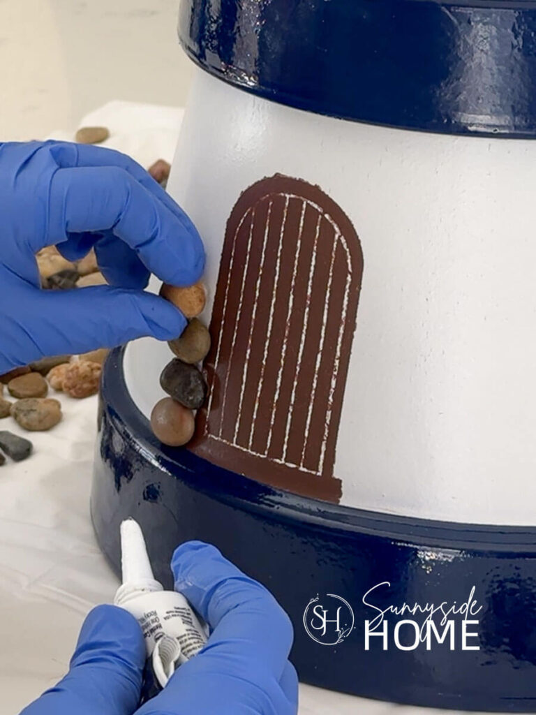Woman adheres pebbles around the door of the clay pot lighthouse with silicone.