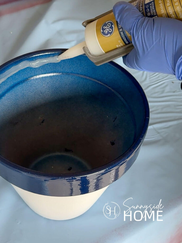 Woman applies a bead of silicone to the inner rim of a painted white and blue clay pot.