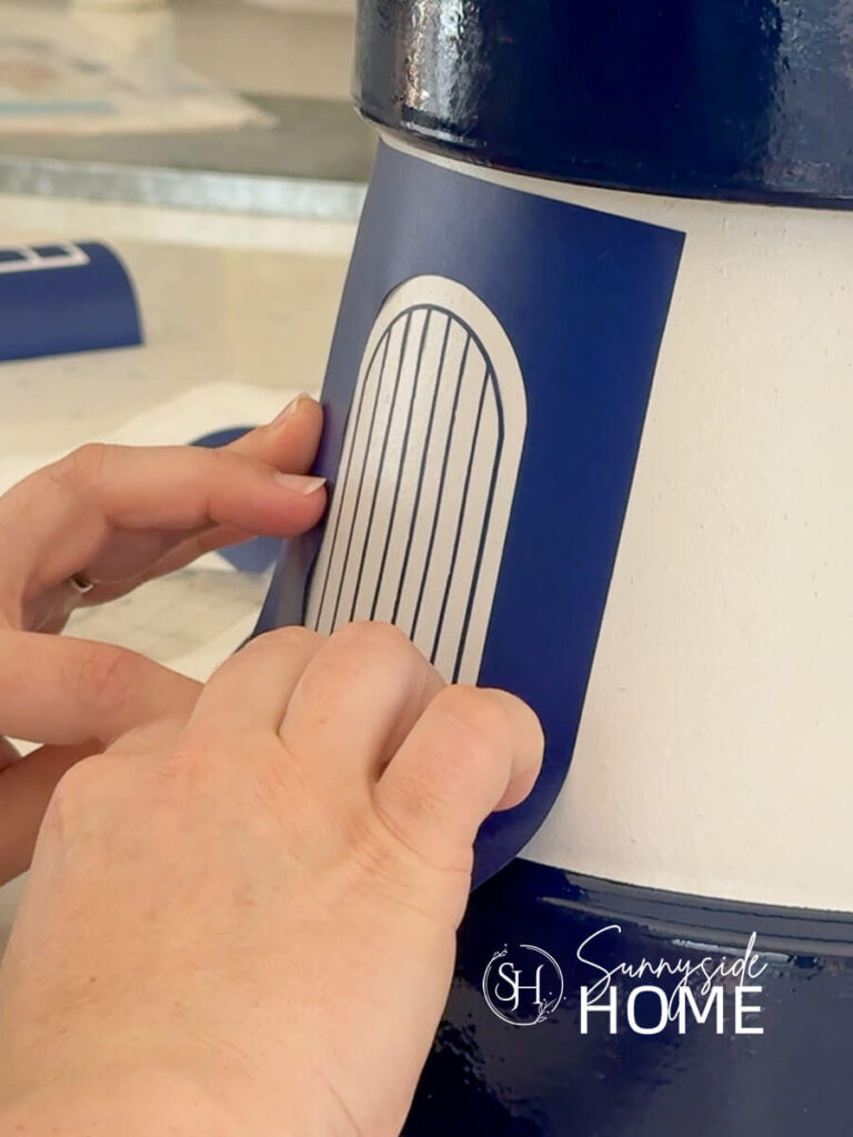 Woman applies a stencil of a door to the clay pot lighthouse.