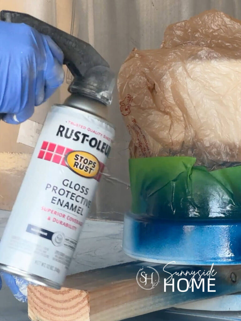 Woman applies navy blue spray paint to a clay pot for the DIY clay pot lighthouse.