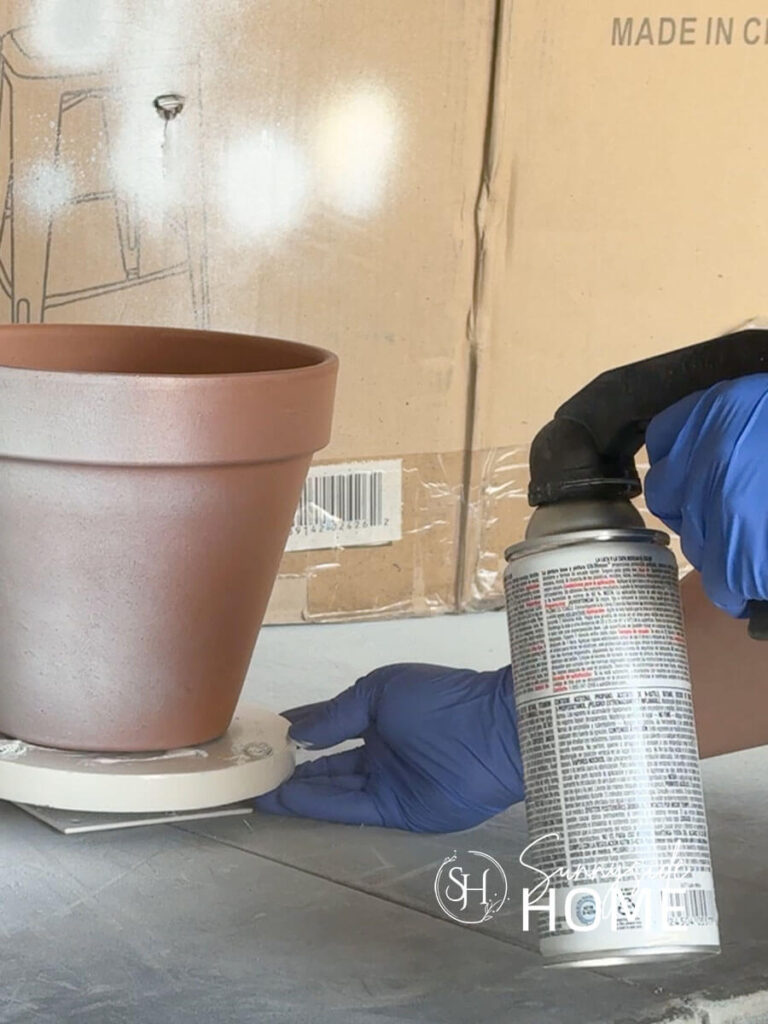 Woman applies a white paint and primer to a clay pot.