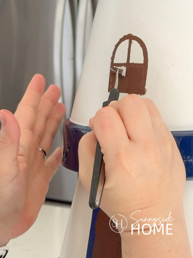 Woman removes the stencil after painting the window on the clay pot lighthouse garden decor.