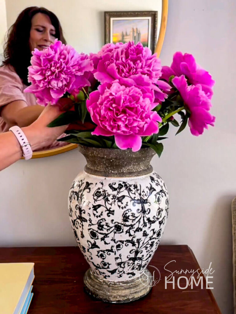 Woman placed pink peonies in a large black and white vase in the entryway.