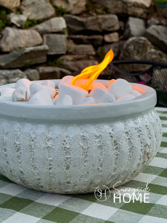 Lit DIY tabletop fire bow on a patio table with a green gingham tablecloth.