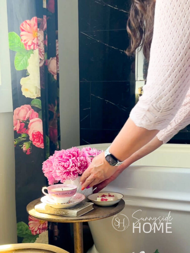 Woman places a bouquet of pink peonies on an accent table in the bathroom.