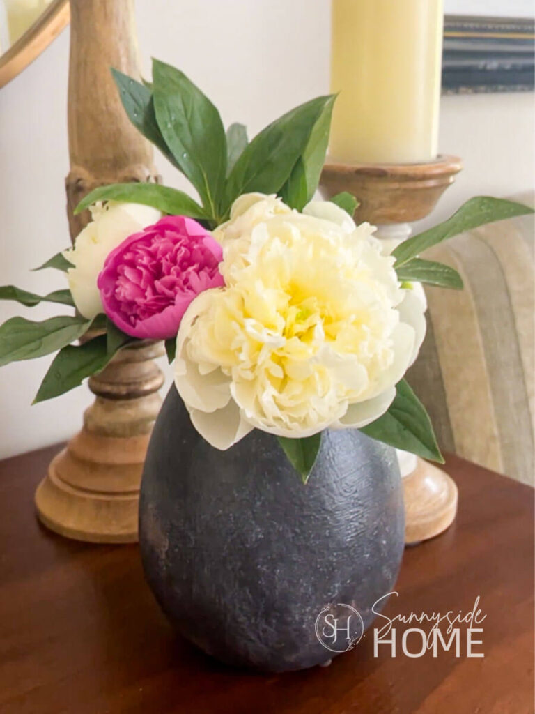 A bouquet of white and pink peonies in a rustic black vase styled with candlesticks.