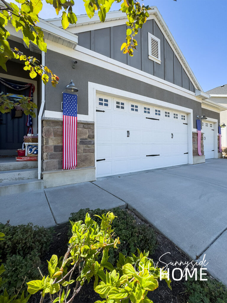 Outdoor fourth of July decorating ideas with red, white and blue flag banners hung from the outdoor lights on each side of the garage doors.