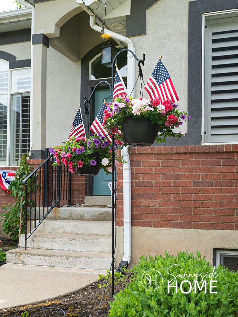 Potted hanging plants are embellished with a pair of American flags in the front yard.